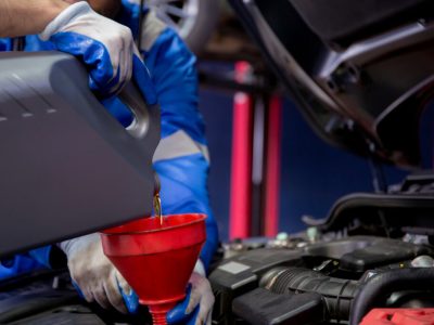 Closeup hands of mechanic man pouring motor oil in engine car in the garage, automobile change lubricant or diesel, worker refilling fluid at auto service, one person, vehicle and transportation.
